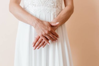 Yakın plan çekimlerde gelinin elleri, beyaz gelinliğinin ince şeftali arkaplanına doğru ince ince ince bağlanmış dantelli detaylarını vurguluyor.