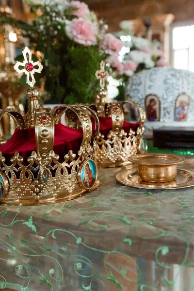 Karmaşık altın taçlar, zengin bir Ortodoks kilisesi içindeki kırmızı kadife yastıkların üzerinde dinleniyor. Bu sahne ruhani otoriteyi simgeleyen kutsal bir taç giyme törenini tasvir ediyor.