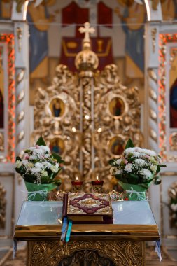 Zengin dekore edilmiş bir Ortodoks Kilisesi sunağında, beyaz çiçek aranjmanları ve açık dini kitaplarla süslenmiş muhteşem bir ikonostaz sergileniyor.