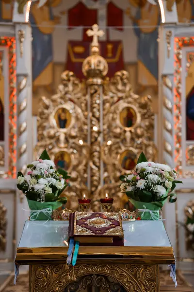 Zengin dekore edilmiş bir Ortodoks Kilisesi sunağında, beyaz çiçek aranjmanları ve açık dini kitaplarla süslenmiş muhteşem bir ikonostaz sergileniyor.