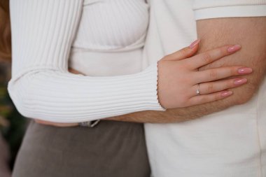 Yakın plan bir çifti şefkatli bir kucaklaşmayla tasvir eder, görünür bir elmas yüzükle sevgi dolu bir bağlılığı simgeler sıcak ve ince bir sevinç sevgiyi ifade eder.