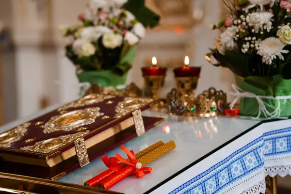 Kırmızı bir İncil, yanan mumlar ve bağlanmış balmumu konikleri içeren, beyaz ve yeşil çiçek desenleriyle süslenmiş zengin bir sunağın yakın çekimi.