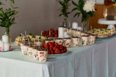 Güzelce düzenlenmiş bir tatlı masasında her bir meyve çeşnisi, taze çilek ve cam vazolarda zarif bir kutlama tarzı sergilenen narin beyaz çiçekler bulunur.