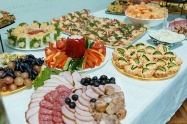 Lezzetli aperatiflerden oluşan geniş bir çeşitlilik. Söğüş et, peynir, taze meyve, sebze atıştırmalıkları ve beyaz bir masa örtüsünün üzerinde güzelce yerleştirilmiş ısırık büyüklüğünde yemekler de dahil.