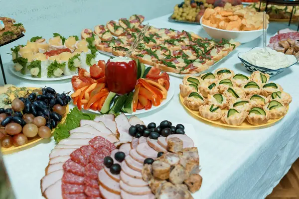 Lezzetli aperatiflerden oluşan geniş bir çeşitlilik. Söğüş et, peynir, taze meyve, sebze atıştırmalıkları ve beyaz bir masa örtüsünün üzerinde güzelce yerleştirilmiş ısırık büyüklüğünde yemekler de dahil.