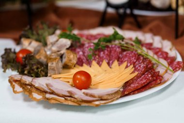 Canlı bir şarküteri tahtasında dilimlenmiş et, peynir, taze domates, maydanoz, marul ve hardal, beyaz bir masa örtüsü üzerinde zarif bir şekilde düzenlenmiş.