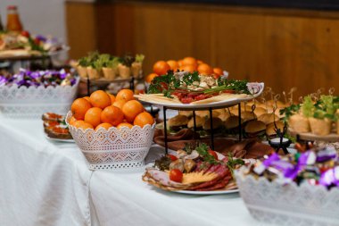 Güzel hazırlanmış yemek büfesi lezzetli aperatifler, renkli meyveler ve beyaz masa örtüsü üzerindeki süslemeler sunar. Kutlamalar için ideal.