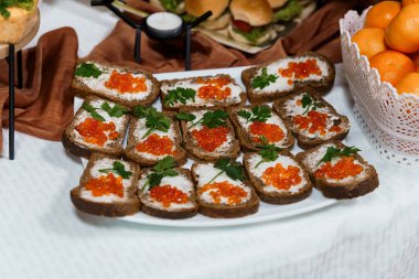 Yakın çekim, kırmızı havyar ve maydanozla kaplanmış çavdar ekmeği dilimlenmiş portakal ve mum ile birlikte sunulan iştah açıcı bir düzenleme sunar.