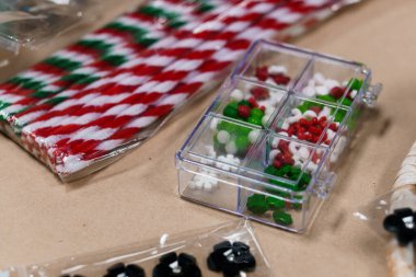 Yakın plan çekimde renkli Noel serpintileri kırmızı ve beyaz kurdelelerle birlikte şeffaf plastik bir konteynıra yerleştirilmiş, tatil pişirme ve el işi projeleri için ideal.