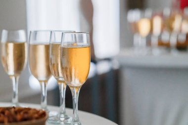 Beyaz bir masada dört şampanya kadehi, bulanık arka planı ve pastaları olan bir kutlama ya da tost öneriyor.