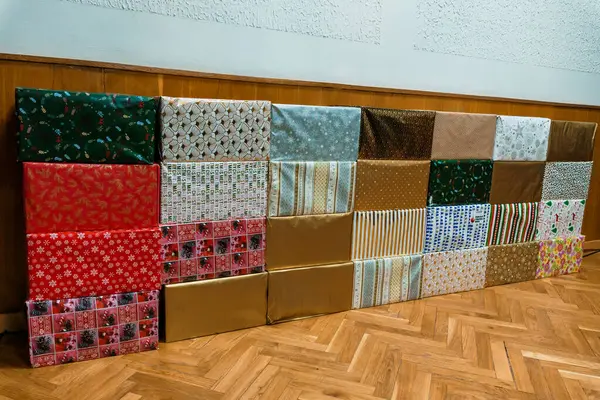 Çeşitli desenlere ve renklere bürünmüş uzun bir sıra parlak Noel hediyeleri basit bir iç dekorda ahşap bir zemin çiziyor. Bu da tatil hazırlığı sahnesini akla getiriyor.