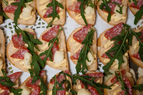 Dilimlenmiş salam, erimiş peynir ve taze roka ile kaplı kızarmış crostini tabağı. Yemek, parti ya da İtalyan mutfağı için mükemmel.