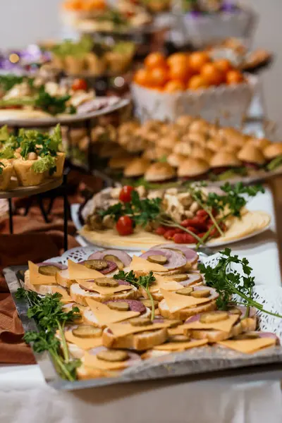 Bu resim peynir, salam, renkli sebzeler, minyatür sandviçler ve etkinlikler için mükemmel taze meyveler içeren çeşitli ordövrlerle dolu pahalı bir büfe masasını gösteriyor.