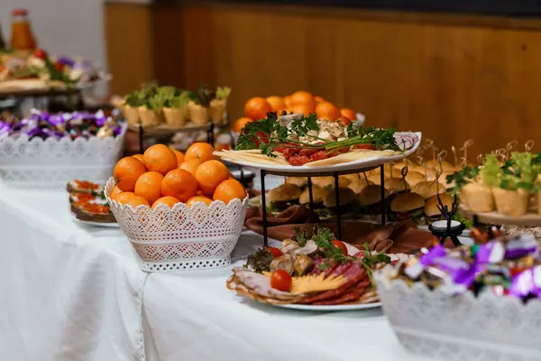 Güzel hazırlanmış yemek büfesi lezzetli aperatifler, renkli meyveler ve beyaz masa örtüsü üzerindeki süslemeler sunar. Kutlamalar için ideal.