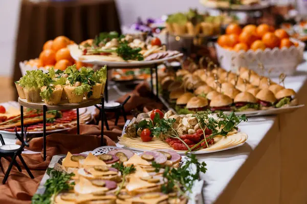 Müsrif bir büfede çeşitli mezeler, şarküteriler, sandviçler ve taze portakallar sergileniyor, katmanlı stantlar ve tabaklar üzerinde sunuluyor, hafif ışıklandırmayla aydınlatılıyor.