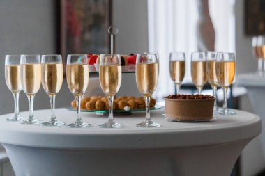 Bir sıra dolu şampanya kadehi, hamur işleriyle dolu bir tatlı masasının yanında oturur. Kutlama toplantısını ya da altın renkli içeceklerle özel bir etkinliği akla getirir.