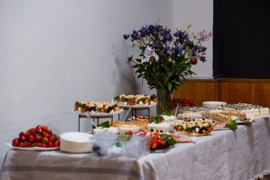 Bol peynir, taze çilek, hamur işleri ve kır çiçekleriyle süslenmiş güzel bir büfe masası davetkar bir ortam yaratır.