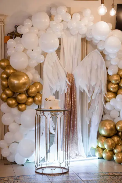 Şatafatlı bir etkinlikte, muhteşem bir beyaz ve altın rengi kemer, melek kanatlarıyla süslenmiş, kutlama ve kilometre taşı etkinlikleri için ideal bir pasta masasını çerçeveliyor.