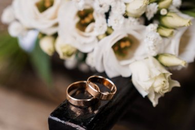 Güzel beyaz bir buketle çevrili karanlık bir yüzeyde duran zarif altın alyansların yakın çekimi aşkı, bağlılığı ve romantik bir olayı simgeliyor.