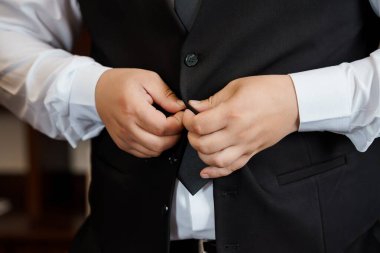 Yakışıklı bir damadın, nikâh törenine hazırlanırken siyah yeleğinin düğmelerini beyaz bir gömleğin üzerine bağladığı yakın plan bir fotoğraf.