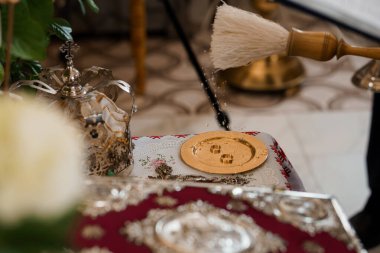 Beyaz çiçeklerle süslenmiş ve kırmızı kumaşın üzerinde dinlenen Ortodoks Hıristiyan düğün ritüeli sırasında Kutsal Komünyon için hazırlanmış karmaşık gümüş paten ve fırça.