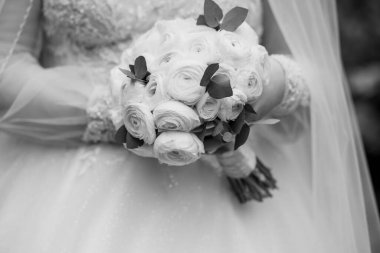 Beyaz güllerden oluşan klasik bir buket tutan bir gelinin yakın plan fotoğrafı, dantelli bir gelinlik ve yumuşak bir duvak, siyah beyaz bir tarz.