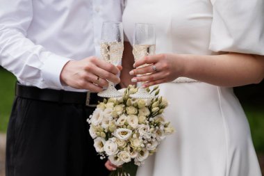 Özel bir düğün sahnesi. Şampanya kadehleriyle kadeh kaldıran, beyaz bir buket tutan, evlilik yüzüklerini gösteren, sevgi, neşe ve bağlılığı somutlaştıran bir çift.