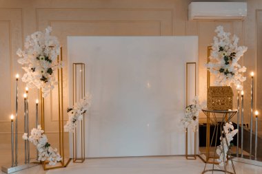 Beyaz çiçekler, altın metal çerçeveler, mumlar ve fotoşoplar ve tören için ideal boş bir arkaplan içeren lüks bir düğün sahnesi dekorasyonu.