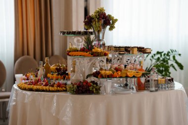 Renkli meyveler, pastalar ve içeceklerle dolu lüks bir tatlı masası. Düğünler, partiler ya da lüks yemek organizasyonları için ideal. Parlak ve davetkar