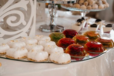 Enfes düğün tatlı masası gösterişli tatlılar, beyaz şekerli kekler, renkli jelatin bardaklar, gümüş tabaklar ve dekoratif öğeler, lüks bir kutlama havası yakalama.