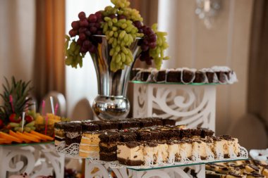 Bol çikolatalı bir pasta, canlı kırmızı üzümler ve çeşitli taze meyveler ile müsrif bir tatlı masası güzelce dekore edilmiş, sofistike bir iç mekan.