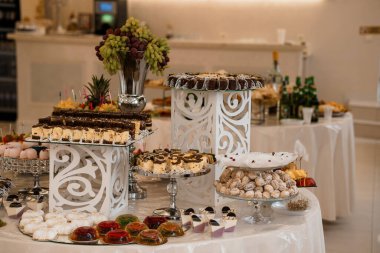 Müsrif bir düğün tatlı sergisi katmanlı çikolatalı kekler, taze üzümler, renkli pastalar ve süslü beyaz stantlar, kutlama ve hoşgörü içeren