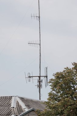 Gri bir tahta çatıya monte edilmiş çok sayıda eski televizyon anteninin yakın plan görüntüsü, bulutlu ve bulutlu bir gökyüzüne karşı modası geçmiş yayın teknolojisini gösteriyor
