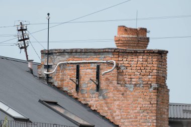 Koyu gri metal çatı boyunca uzanan boruları olan, eskimiş bir gökyüzü arkaplanı olan eskimiş bir estetiği gösteren, yaşlanmakta olan tuğladan bir bacanın yakın plan görüntüsü.