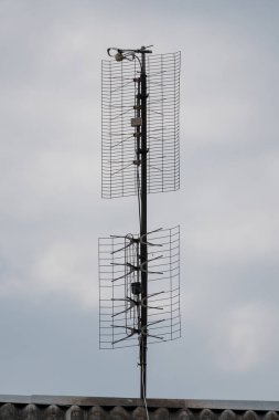 Yıpranmış gri bir televizyon anten sistemi fayanslı bir çatıya monte edilmişti. Bulutlu ve bulutlu bir gökyüzüne karşı sinyal alıcısını geliştirmek için iki üst üste yığılmış anten sergiliyordu.