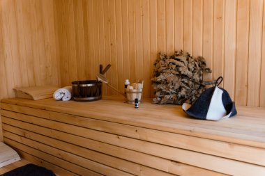 Konforlu Finlandiya sauna odasının içinde ahşap banklar, metal bir kova, çırpılmış havlular ve huzur ve rahatlık için huzurlu bir spa atmosferi yaratan şapkalar bulunur.