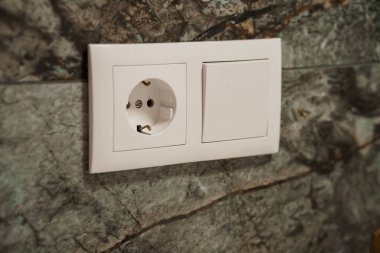 An image showcasing a clean white electrical outlet and light switch set against a gray marble wall, representing home interiors, power supply, and modern design