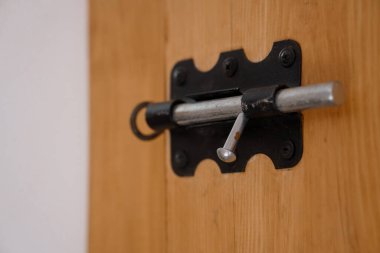 Detailed view of a black metal barrel bolt latch secured on a light brown wooden door, showcasing a simple home security feature with rustic charm. ideal for interior design concepts, farmhouse style, or hardware illustrations