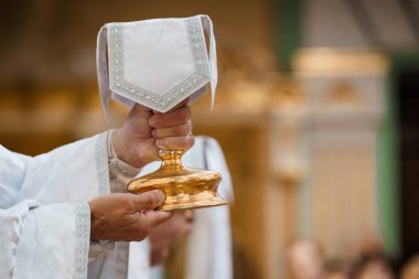 Katolik bir rahip, kutsal ayin ayinini içeren kadehi zengin altın kaplamalı bir kilisenin içinde kutsal bir törenle yükseltiyor.
