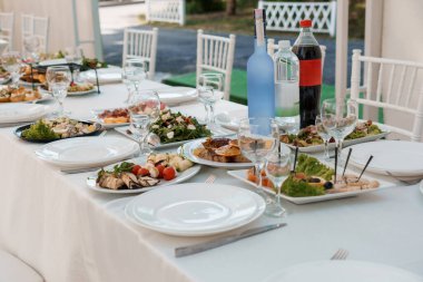 Şatafatlı düğün masası çeşitli aperatifler, köpüklü şarap şişeleri, kristal bardaklar ve beyaz çarşaflar ile güzelce düzenlenmiştir. Organizasyon ya da yemek servisi için mükemmeldir.