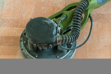 Yakından bakıldığında, kırsal ahşap bir zeminde duran zeytin yeşili, rastgele bir elektrik yörünge zımparalayıcısını, zımparalamak, tamir etmek ve bitirmek için kullanılan yaygın bir DIY ev yenileme aracını gösteriyor.