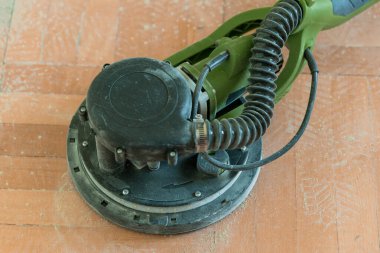 Yakından bakıldığında, kırsal ahşap bir zeminde duran zeytin yeşili, rastgele bir elektrik yörünge zımparalayıcısını, zımparalamak, tamir etmek ve bitirmek için kullanılan yaygın bir DIY ev yenileme aracını gösteriyor.