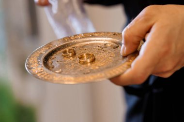 Ortodoks Hıristiyan nikah törenine yakın plan. Bir rahip, evlilik yüzükleriyle altın paten takıyor. Kutsal birlikteliği ve bağlılığı simgeliyor.