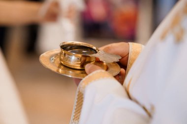 Bir rahip, Katolik ayini sırasında şarap eşliğinde altın bir kadeh tutuyor. Bulanık bir kilise arkaplanı ve sıcak bir aydınlatma ile kutsal bir dini anı yakalıyor.