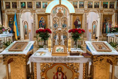 Bir Doğu Ortodoks kilisesinde zengin dekore edilmiş bir sunak, azizlerin ikonları, yanan mumlar, canlı kırmızı güller, altın süslemeler ve kutsal bir atmosfer yaratan dini yazıtlar sergileniyor.