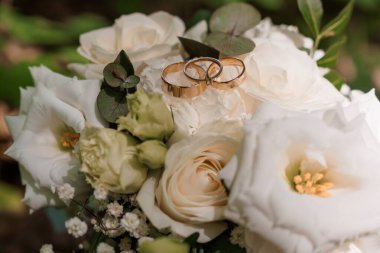 Yakından çekilen iki altın alyans yemyeşil bir gül buketinin üzerinde duruyor. Aşkı ve bağlılığı sembolize ediyor. Düğün temaları için mükemmel.