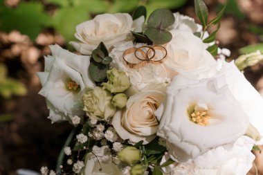 Altın alyansların yakın plan görüntüsü gür, beyaz gül buketi içinde okaliptüs yapraklı, aşkı, bağlılığı ve romantik bir kutlamayı simgeliyor.