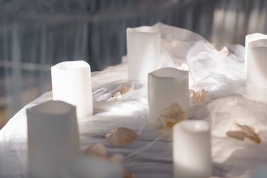 Zarif beyaz bir masa örtüsü üzerine serpiştirilmiş gül yaprakları arasına dağılmış, alevlenmemiş beyaz sütun mumlarıyla süslenmiş, yumuşak ve samimi bir ruh hali yaratan huzurlu bir düğün masasının yakın çekimi.