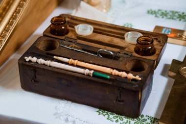 İçinde neşterler, damlalar ve siyah bir kutunun içindeki aletlerin bulunduğu titizlikle hazırlanmış antika bir tıbbi malzeme beyaz dantelli bir kumaşın üzerinde duruyor, tarihi sağlık uygulamalarını çağrıştırıyor.