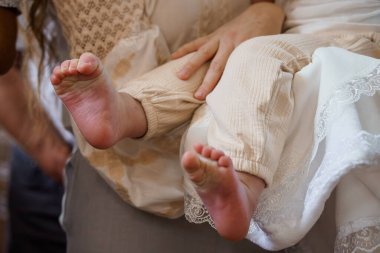 Yakın plan, yumuşak odaklı fotoğraf sergileniyor. Küçük bebek ayakları sevgiyle tutuluyor, kurdeleli bronz elbiseler giyiyor ve dantelli, detaylı bir elbise giyip şefkat uyandırıyor.